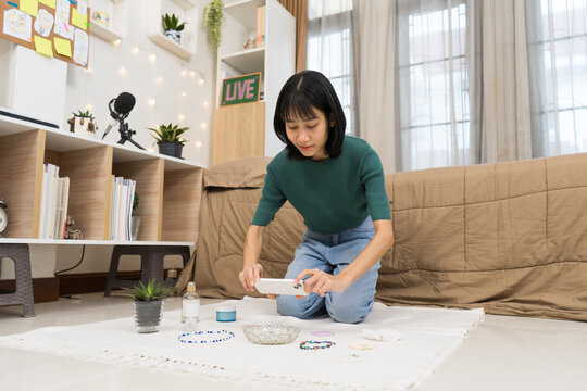 Young  woman Styling and Photographing smartphone to photograph  jewelry on a clean white backdrop in home studio r Online Store