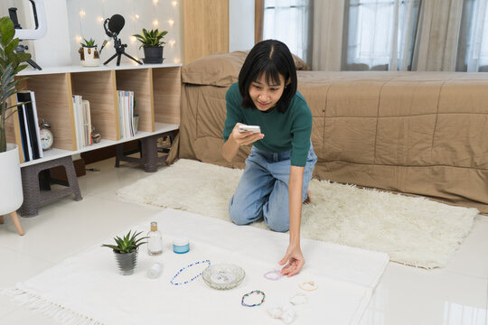 Young  woman Styling and Photographing smartphone to photograph  jewelry on a clean white backdrop in home studio r Online Store