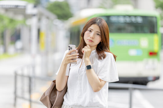 スマートフォンを見ながら悩む日本人女性とバス停の風景