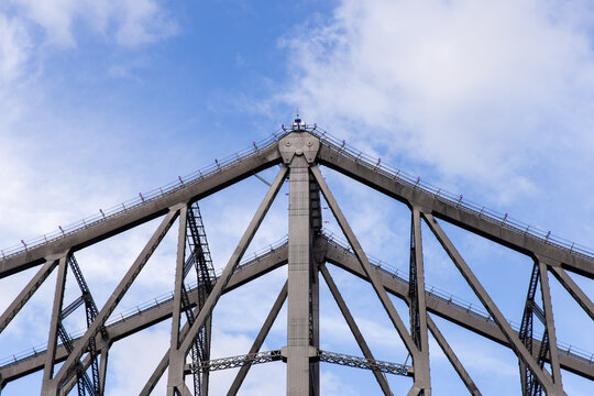 close up of the top point of the Story Bridge in the sun against a blue sky with some white clouds