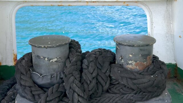Mooring Ropes and Bollards on Ferry Deck. Thick mooring ropes wrapped around metal bollards on a ferry deck with blue sea water in the background. Nautical equipment and maritime transport detail.