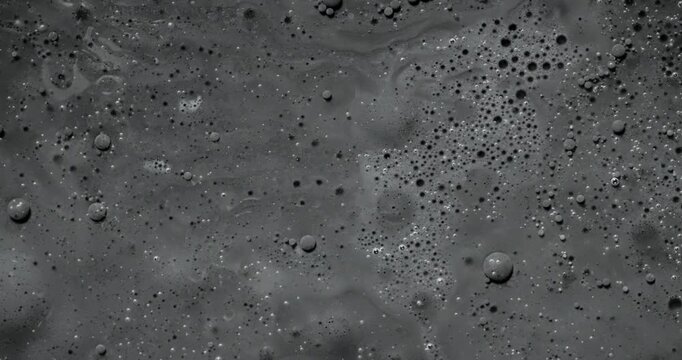 Black bubbly liquid rotation. Close-up of dark viscous surface with dense foam and bubbles. Smooth continuous rotation reveals shifting patterns and light reflections.
