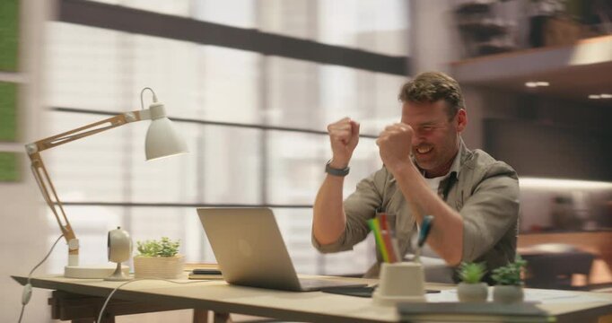 360 Degree. Man Types on Laptop Then Celebrates Productivity Boost With Raised Fists and Smile in Office, Optimising Workflow and Reaching Business Goal at Desk. Orbital Cinematic Arc Tracking Shot.