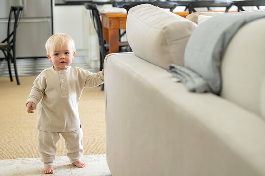 Toddler boy holding onto a light coloured couch
