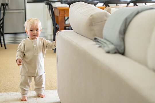 Toddler boy holding onto a light coloured couch