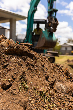Close-up view of freshly dug soil in the foreground with a teal excavator in the background