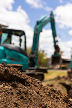 Close-up view of freshly dug soil in the foreground with a teal excavator in the background