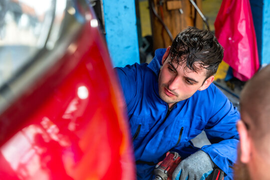 Handsome  male auto mechanic in uniform focusing on repairing and maintaining car engine in well equipped automotive repair shop