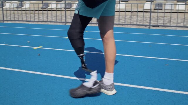 Man sprinter with bionic leg prosthesis walks along empty track