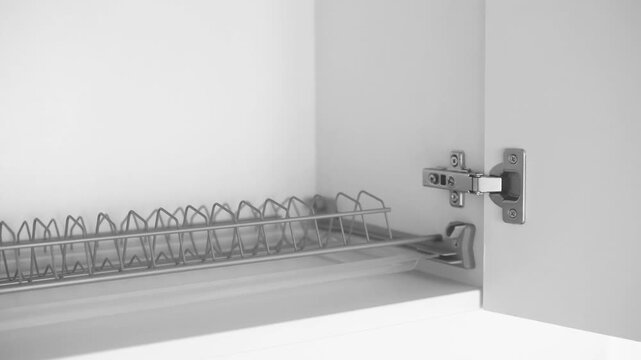 Metal dish rack inside an open white cabinet with a hinge