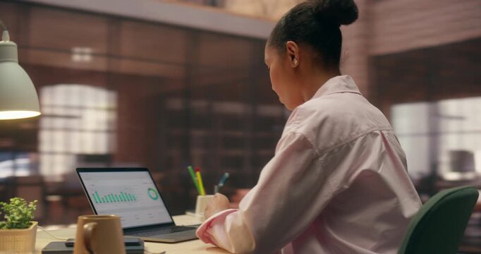 360 Degree. Young Mixed Race Woman Works on Laptop in Office, Analyzing Ecommerce Data and Sales Charts, Smiling Confidently While Researching Business Growth and Payment Software.  Arc Tracking Shot.