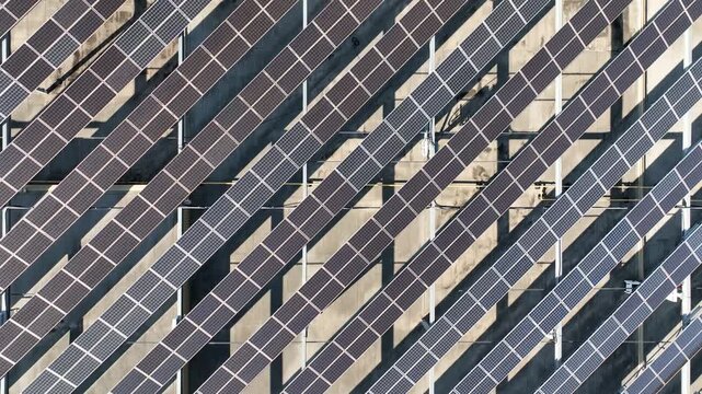 Drone aerial view of large-scale rooftop solar panel arrays on industrial building in a manufacturing district. The drone is rising up from the center point to gradually reveal the full array.
