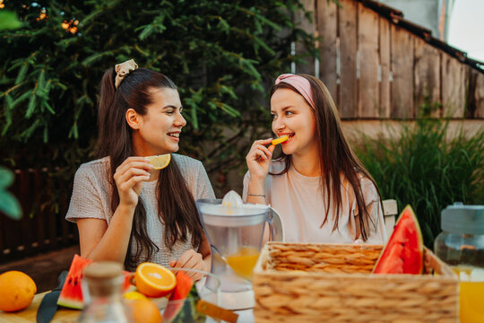 Young women enjoying fresh fruit and making orange juice outdoors