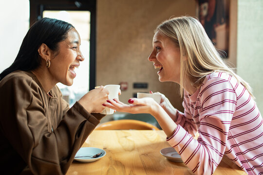 Two friends laughing over coffee at cafe table