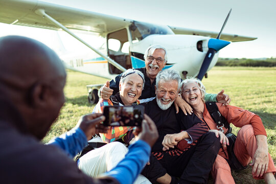 Senior friends taking photo in skydiving gear by small airplane at airfield