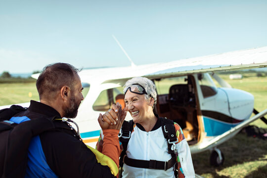 Instructor congratulates senior skydiver beside small plane