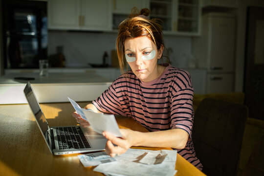 Woman wearing eye patches paying bills at home kitchen table