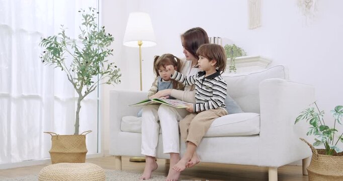Mom raises finger, points object, explains new word, brother repeats, sister listens, book rests on knees, homeschooling preschool learning game unfolds in livingroom, gentle parenting vibe.