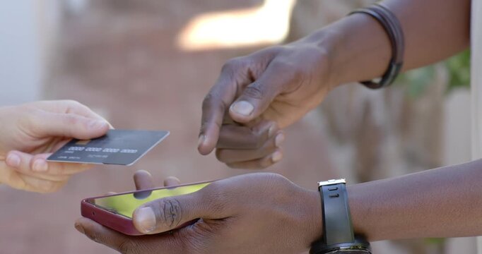 Diverse adults presenting dark payment card, man tapping red-cased smartphone on brick walkway