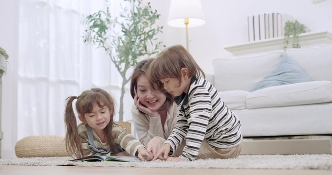 Single mother sits on floor with preschool son, toddler daughter, helping sibling learning game, kid points at picture book pages, homeschool moment, social skill growth, supportive parenting, home.