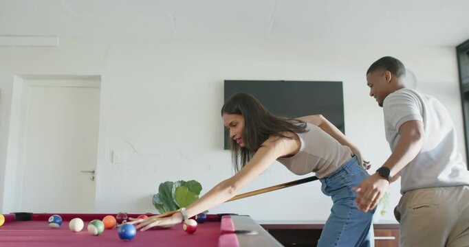 African American couple leaning at red-felt table, man reaching for cue while woman aiming balls
