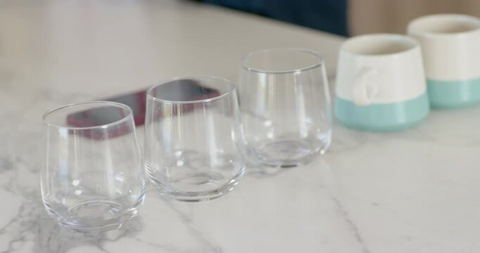 Camera adjusting focus stabilizing, 3 glasses shifting on marble top, phone under left, mugs right