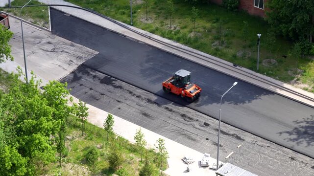 Road resurfacing work with a compact construction roller machine laying fresh asphalt on urban street during infrastructure maintenance and road repair works