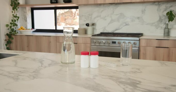 Carafe, two white bottles, glass are sitting on countertop as camera is moving to reveal shelf