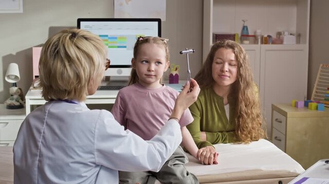 Eye level medium shot of Caucasian female pediatrician performing neurological reflex test on Caucasian girl sitting with mother. Perfect for pediatric clinic promotions, family healthcare marketing
