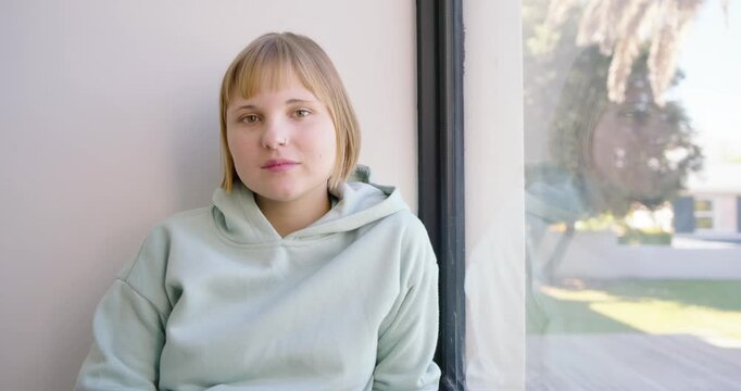 Woman in mint hoodie sitting by large vertical window, daylight causing head tilts and gaze shifts