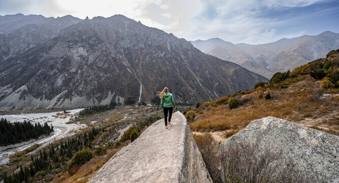 View of the Ala Archa valley from the viewpoint, hiker on a large rock, Broken Heart Rock, autumnal mountain landscape, mountain stream Ak Say and Ala Archa, Ala Archa National Park, Khirgiz Ala-Too Mountains, Chuy Region, Kyrgyzstan