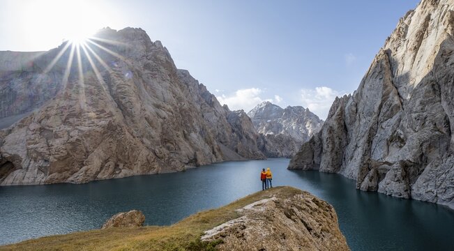 Couple at the blue mountain lake between rocky steep mountain peaks, Sun Star, Kol Suu Lake, Sary Beles Mountains, Naryn Province, Kyrgyzstan