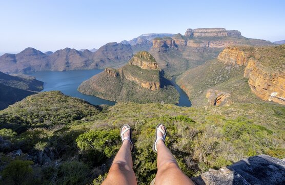 Legs of a sitting woman, view of river bend at Blyde River Canyon with Three Rondawels peak, view of canyon with Blyde River and table mountains in the evening light, canyon landscape, Panorama Route, Mpumalanga, South Africa