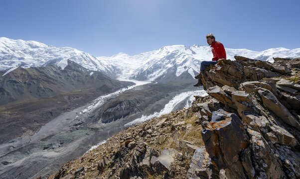 Mountaineer at Traveller's Pass with view of impressive mountain landscape, high mountain landscape with glacier moraines and glacier tongues, glaciated and snow-covered mountain peaks, Lenin Peak and Peak of the XIX Party Congress of the CPSU, Trans Alay Mountains, Pamir Mountains, Osh Province, Kyrgyzstan