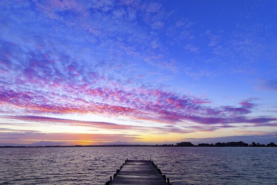 A footbridge leads into Lake D&uuml;mmer, above it a colorful sky at sunset, D&uuml;mmer nature park Park, Lembruch, Lower Saxony, Eutschland