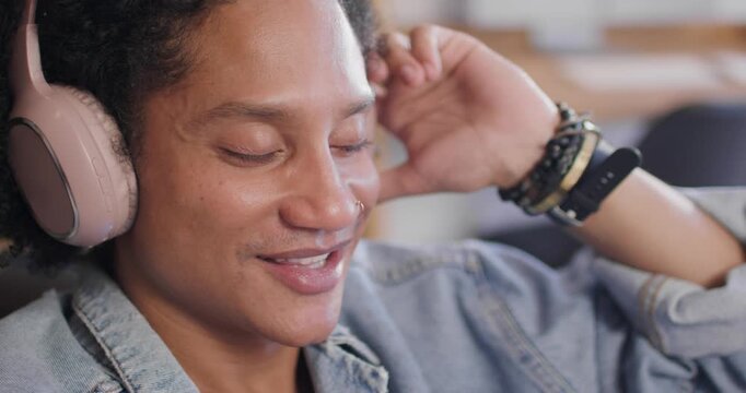 African American man hearing music, sitting in lounge, mouthing lyrics and adjusting headphones