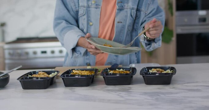 African American man scooping from plate with fork, filling four boxes in kitchen, meal prepping