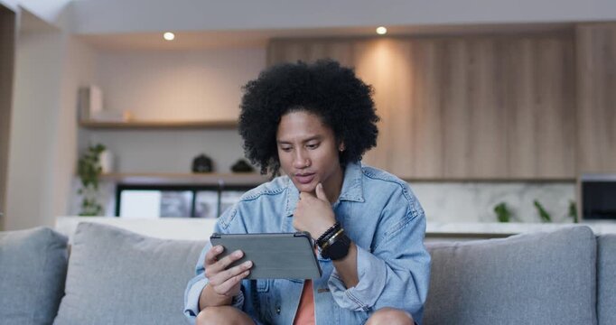African American man holding tablet, leaning, tapping and swiping while reading content on sofa