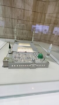 A detailed, illuminated scale model of the Prophet's Mosque (Al-Masjid an-Nabawi) featuring the iconic Green Dome on display in a museum.