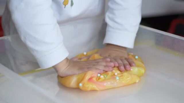 Close-up of hands pressing colorful slime with foam beads. Educational sensory activity illustrating tactile perception, creativity, concentration and motor skill development.