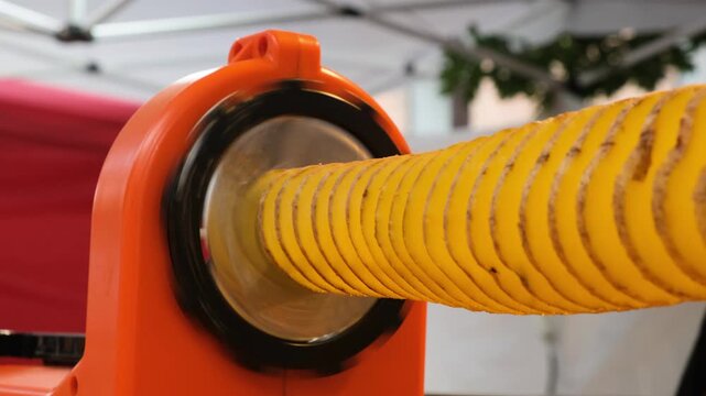 Electric potato twister machine transforming a whole potato into a tornado potato spiral. Preparing popular street food snack using automatic spiral cutting technology in a kitchen setting.