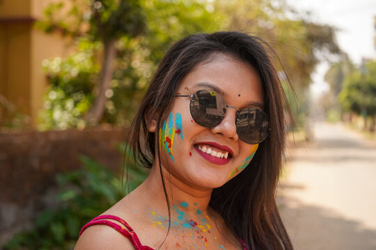 Indian young woman smiles with colorful face looking at camera wearing sunglasses in Holi. concept of Indian Holi festival.