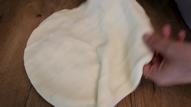 a person presses and shapes raw pie dough edges by hand on a wooden table in a home kitchen during baking preparation to seal and form a pie