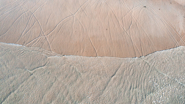 Aerial view of intricate water patterns and tracks on a sandy beach with shallow clear water washing over the shore in Perranporth, Cornwall, United Kingdom.