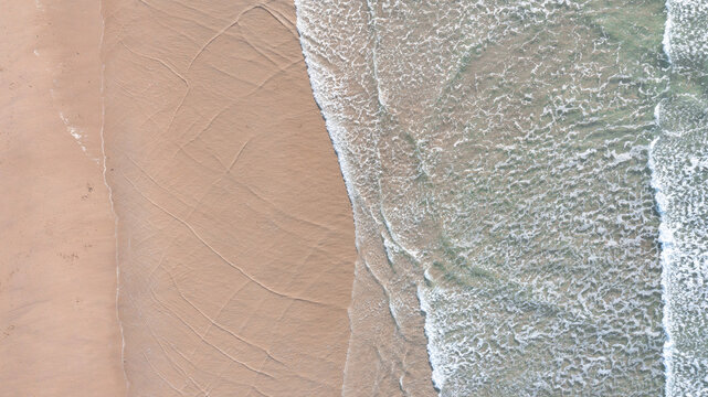 Aerial view of gentle waves washing over the sandy shoreline of Perranporth beach in Perranporth, Cornwall, United Kingdom.