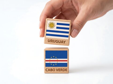 Hand holding Uruguay flag wooden block above Cabo Verde block