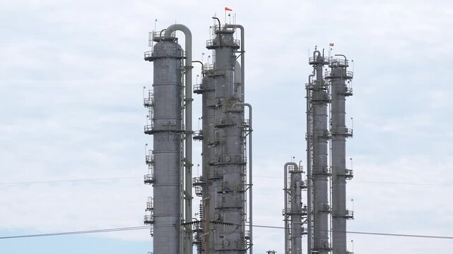 Industrial refinery distillation column tower pipeline engineering inspection, petrochemical processing plant with tall fractionator stack, valve network, ladder platform, overcast sky, oil and gas