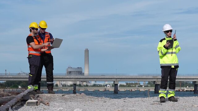 Engineer inspection industrial engineering safety hardhat visibility laptop tablet radio team conducting waterfront bridge construction site survey and compliance check, documenting data
