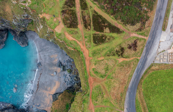 Aerial view of Hell's Mouth coastal cliffs with turquoise water, sandy beach, and dirt paths on the grassy clifftop near a road Camborne, Cornwall, United Kingdom.