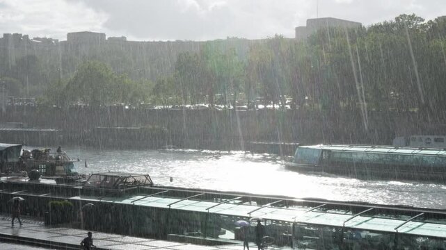 A glass passenger cruise boat navigates the Seine River during a heavy summer rainstorm in Paris France. European city travel tourism under a downpour, wet weather holiday voyage transit.